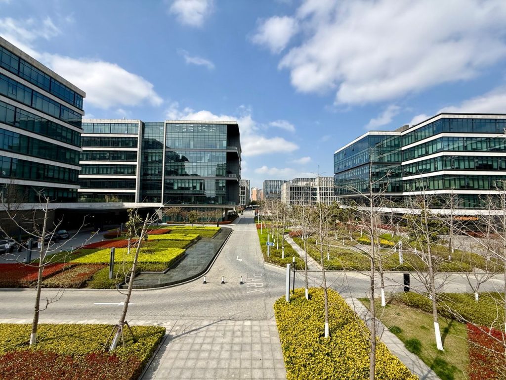 A vibrant modern business district featuring sleek buildings and lush gardens under a blue sky.